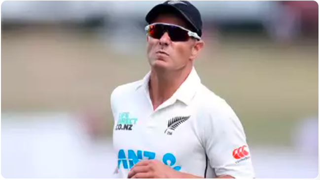 Neil Wagner, a cricket player in white attire, holding a cricket ball, appears reflective as he walks back to his mark on the field.