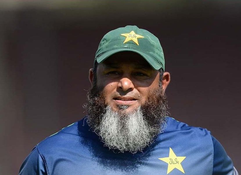 Mushtaq Ahmed, wearing a Bangladesh team jersey, gestures while holding a cricket ball.